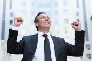 Everyday winner. Happy senior man in formalwear keeping arms raised and expressing positivity while standing outdoors photo