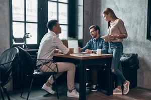 Group of young modern people in smart casual wear discussing something while working in office photo