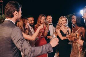 grupo de personas en ropa formal comunicándose y sonriendo mientras pasan tiempo en una fiesta de lujo foto