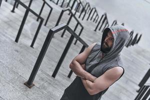 Feeling confident. Handsome young man in sport clothing keeping arms crossed while standing on the steps outside photo