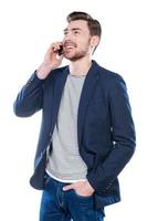 Good talk with friend. Handsome young man talking on the mobile phone and smiling while standing against white background photo