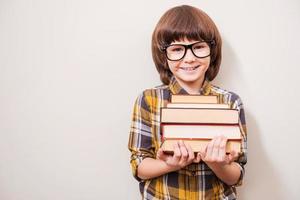 I love reading Happy little boy holding book stack and smiling while standing against grey background photo