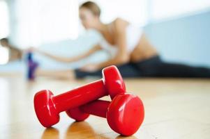 Sport and fitness concept. Close up image of dumbbell lying on the floor while young woman stretching on background photo