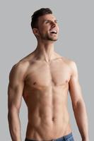 Reviving his energy. Handsome young muscular man shouting and looking away while standing isolated on grey background photo