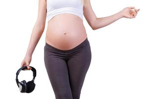amamos la música. imagen recortada de una mujer embarazada sosteniendo auriculares mientras está aislada en blanco foto