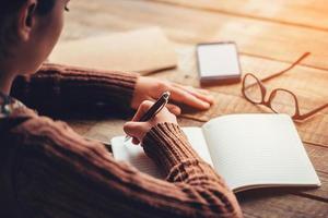 Making notes. Close-up image of woman writing in notebook with copy space while sitting at the rough wooden table photo