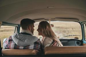 haciéndonos felices unos a otros. hermosa pareja joven que se une y sonríe mientras se sienta en los asientos del pasajero delantero en una mini furgoneta de estilo retro foto