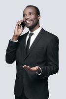 Best decisions. Handsome young African man in suit talking on the phone and gesturing while standing against grey background photo