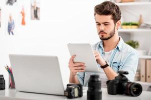 Finding a right photo for his project. Confident young man working on digital tablet while sitting at his working place