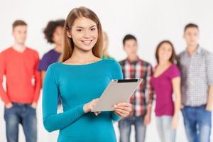 Join a digital age. Cheerful young woman holding digital tablet while his friends standing on background photo