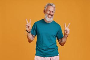 Happy senior man gesturing and smiling while standing against orange background photo