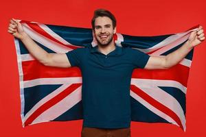 Handsome young man in casual wear carrying British flag and smiling photo