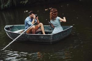 Nice shot. Young man photographing his beautiful girlfriend while enjoying romantic date on the lake photo