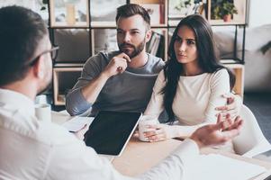 necesitan asesoramiento de expertos. pareja joven sentada en el escritorio y escuchando a su asesor financiero foto