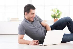 Surfing the net at home. Cheerful young man lying on the floor and using computer photo