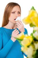 Woman sneezing. Young woman holding handkerchief near face and sneezing while standing isolated on white photo