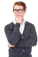 In search of new creative ideas. Thoughtful young man holding hand on chin and looking away while standing isolated on white photo