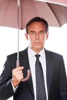 hombre de negocios con paraguas. hombre maduro confiado en ropa formal sosteniendo paraguas y mirando a la cámara mientras está de pie contra el fondo blanco foto