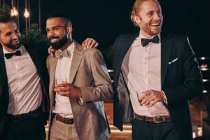 Three handsome men in suits bonding and drinking whiskey while spending time on party photo