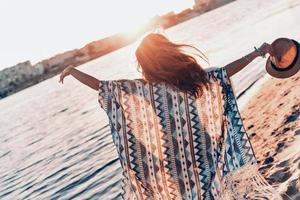 Feeling the freedom.  Rear view of young woman in sarong keeping arms outstretched while standing on the beach outdoors photo