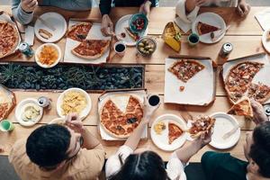 Favorite food. Close up top view of young people eating pizza while having a dinner party indoors photo