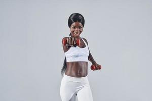 Beautiful young African woman in sports clothing exercising with dumbbells photo