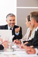 Good news for our company Business people in formalwear discussing something while sitting together at the table photo