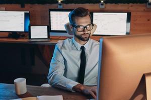 Confident young man working on computer while staying late in the office photo
