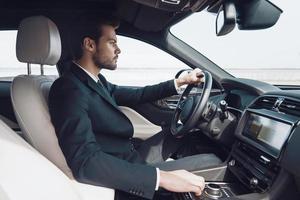 Time is money. Handsome young man in full suit looking straight while driving a car photo