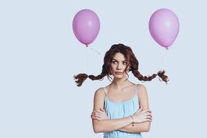 Calm and beautiful. Studio shot of beautiful young woman with balloons tied to her pigtails looking away while standing against grey background photo