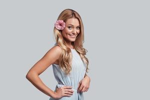 Perfect beauty. Attractive young woman with a flower in hair looking at camera and smiling while standing against grey background photo