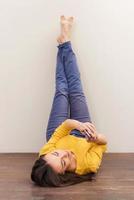 Beauty with mobile phone. Beautiful young woman holding mobile phone while lying on the floor and leaning her legs at the wall photo