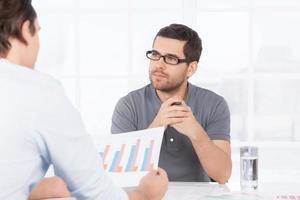 Going over the numbers. Two confident business people in casual wear discussing something while one of them holding a paper with graph on it photo