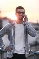 Sharing good news. Handsome young man in eyewear talking on the mobile phone while standing outdoors photo