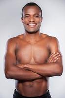 Confidence and masculinity. Young African man looking at camera and keeping arms crossed while standing isolated on grey background photo