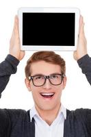 Copy space on his tablet. Cheerful young man holding a digital tablet upon his head and smiling while standing isolated on white photo