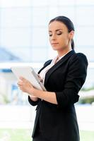 Freedom to work everywhere. Confident young woman in formalwear working on digital tablet while standing outdoors photo