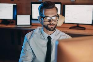 Confident young man working on computer while staying late in the office photo