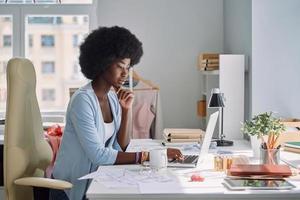 Beautiful young African woman using laptop while working in design studio photo