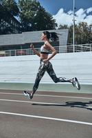 siempre en una gran forma. toda la longitud de una mujer joven con ropa deportiva trotando mientras hace ejercicio al aire libre foto