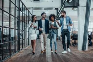 Creative business on the move. Full length of young colleagues in smart casual wear walking and talking during a coffee break at work photo