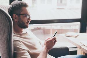 Business message. Side view of handsome man using his smartphone while sitting in chair in front of window photo
