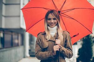 Join me under my umbrella Attractive young smiling woman carrying umbrella and looking at camera while standing on the street photo