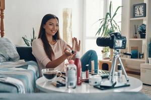 Attractive young woman pointing at beauty product and smiling while making social media video photo
