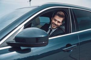 Happy driver. Handsome young man in full suit looking straight while driving a car photo