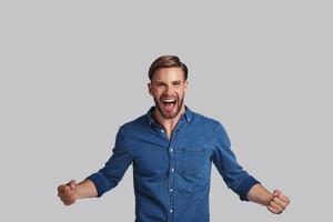 Handsome young man gesturing and looking at camera with smile while standing against grey background photo