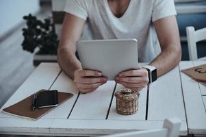 Perfect place to work. Close-up of young modern man wearing smart watch and holding digital tablet while sitting at the table photo