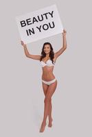 Always believe in yourself.  Full length of attractive young woman holding a poster and looking at camera with smile while standing against grey background photo