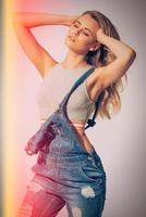 Feeling casual. Studio shot of beautiful young woman in jeans overall holding hands in hair and keeping eyes closed photo