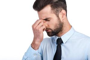 Feeling stressed. Frustrated young man in shirt and tie massaging nose and keeping eyes closed while standing against white background photo